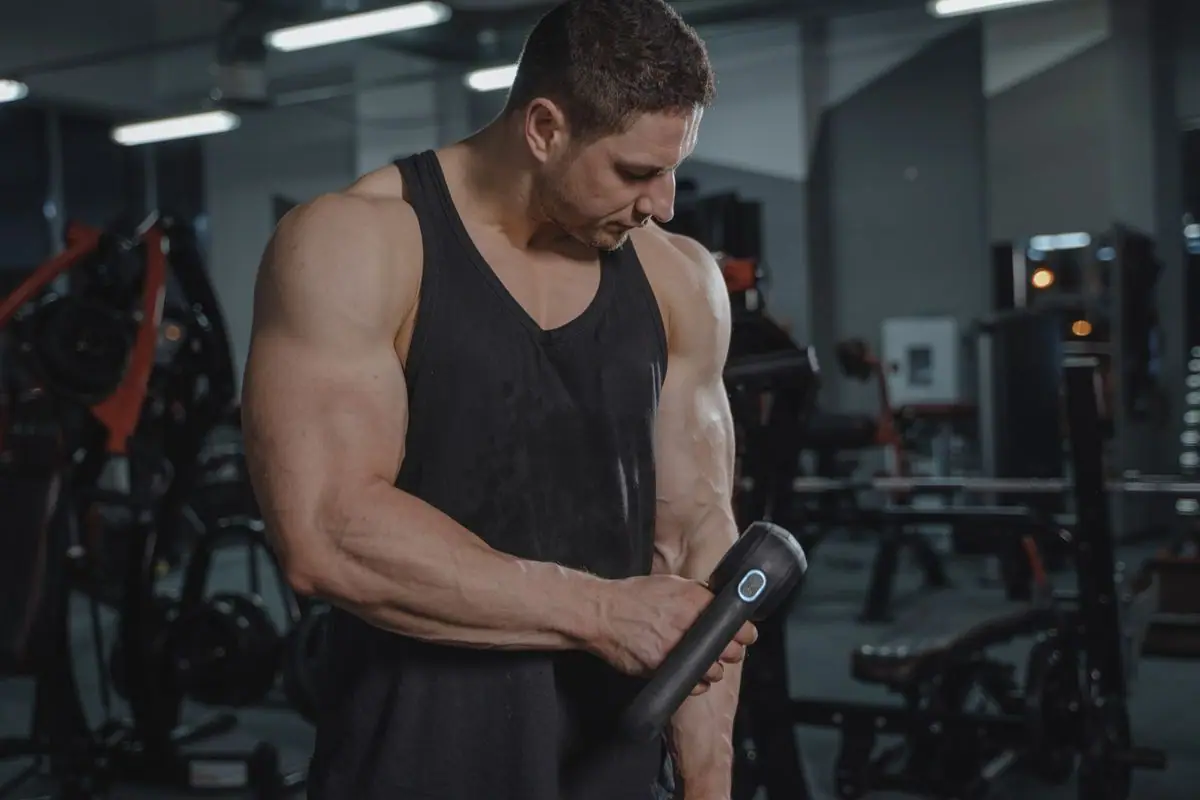 A man using a percussion massage gun at the gym