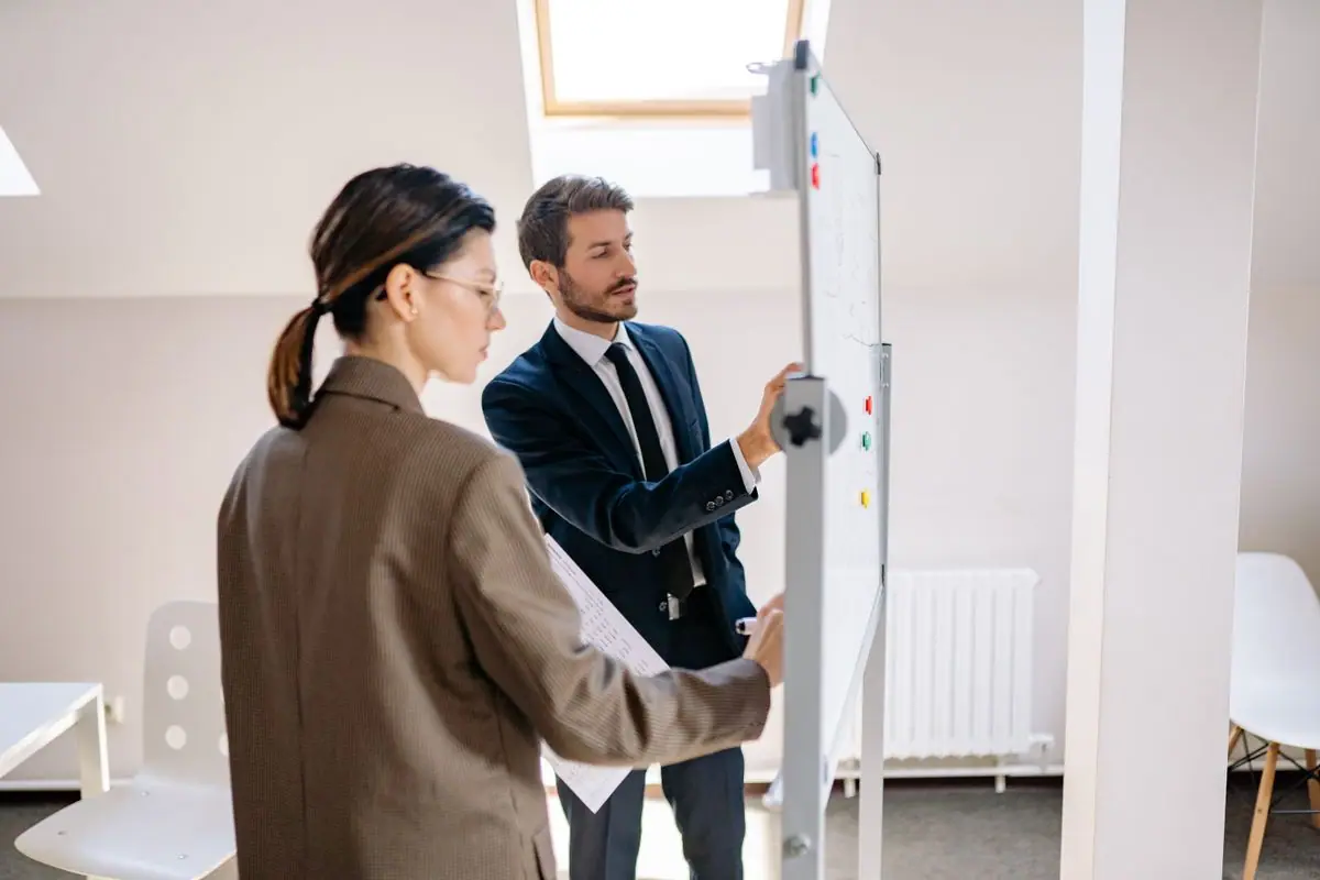 Two colleagues writing on an office whiteboard