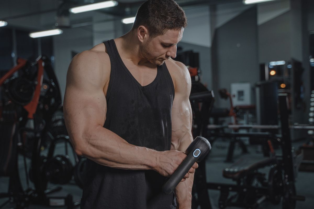 A man using a percussion massage gun at the gym