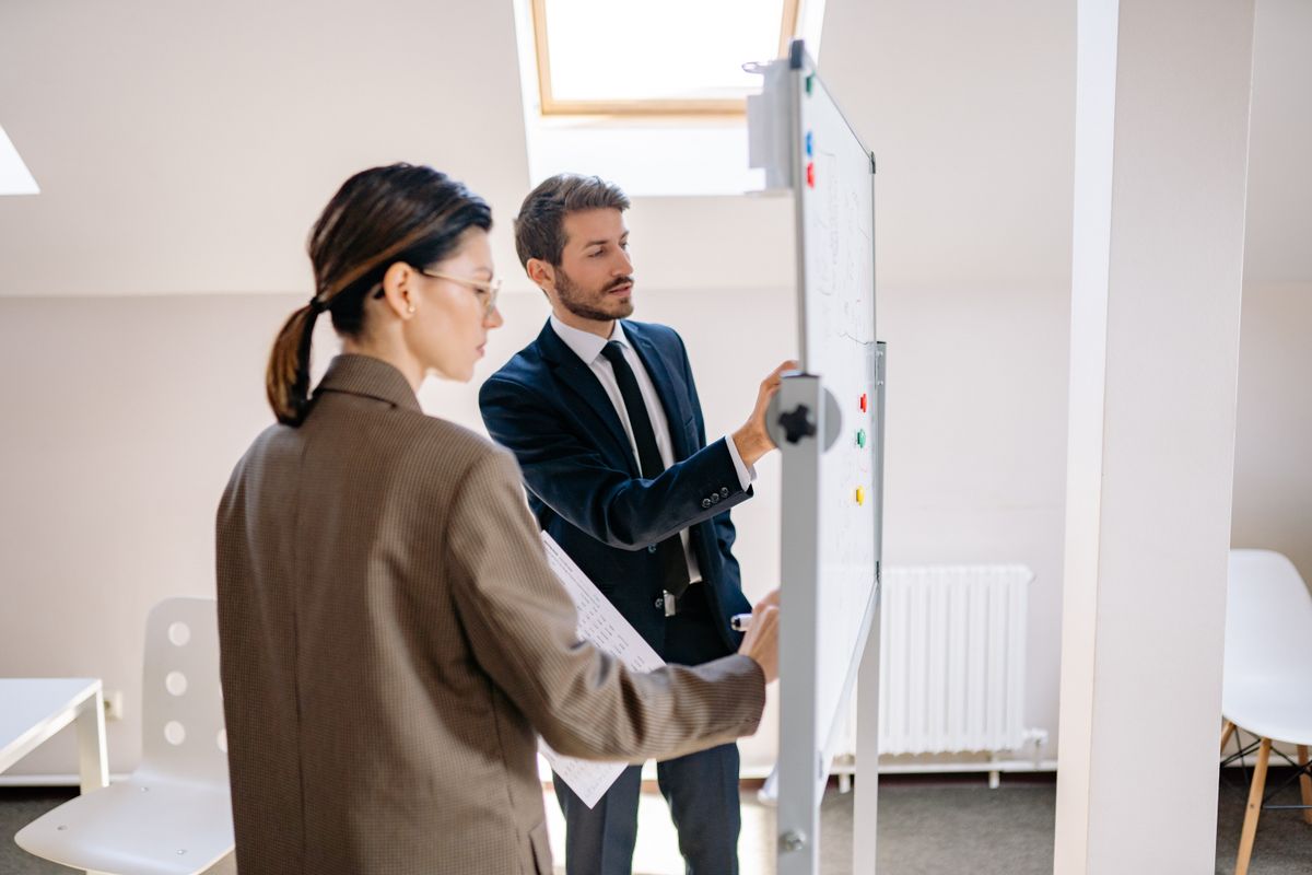 Two colleagues writing on an office whiteboard